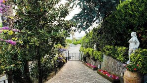 A paved pathway with a decorative pattern, flanked by lush greenery and a statue. - Villa Angela with private pool and sea view (Priora)