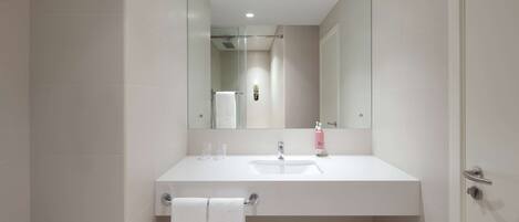A modern bathroom with a white sink, mirror, and glass shower enclosure.