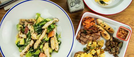A table with three plates of food, including a salad, eggs benedict, and a variety of meats and potatoes.
