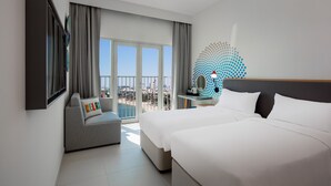 A hotel room with a balcony, a sofa, a bed, a desk, and a decorative wall piece. - Rove La Mer Beach (Dubai)