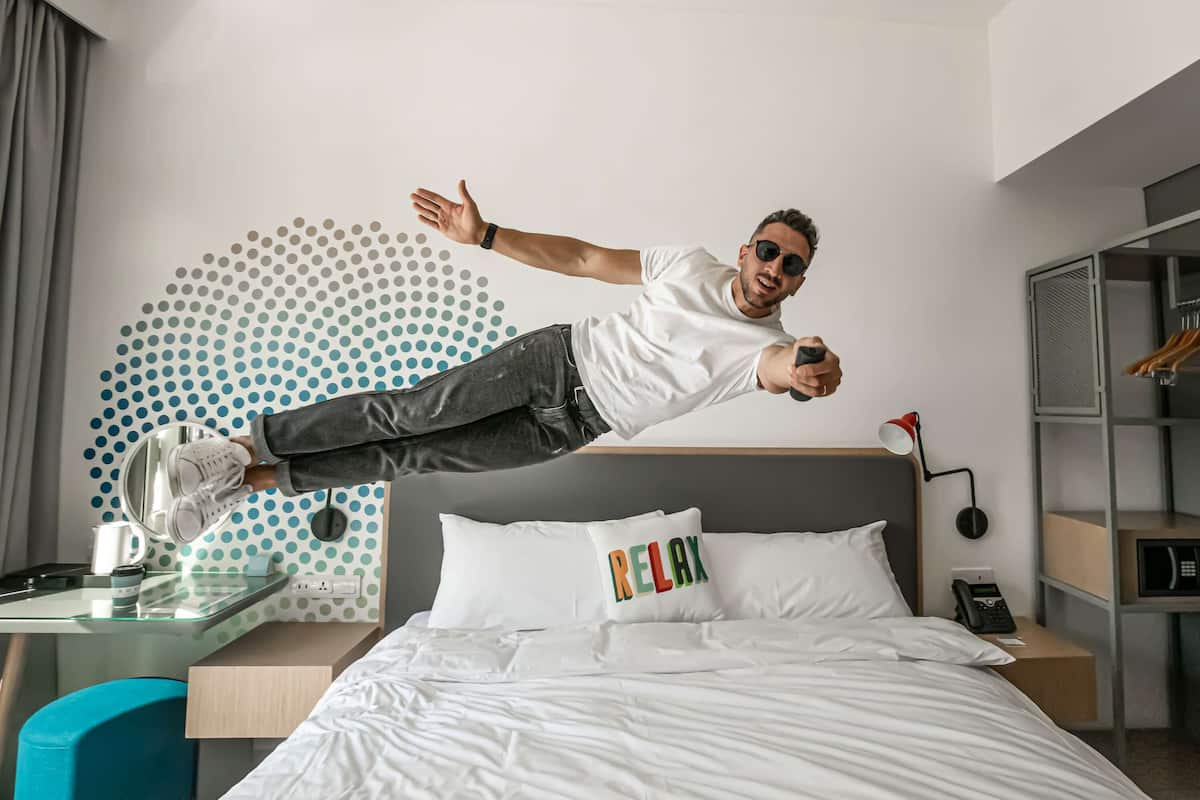 A person jumping in a modern hotel room with a bed, a desk, and a wall with a polka dot pattern.