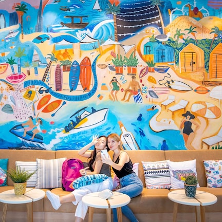 A vibrant mural with beach and tropical elements, a sofa with colorful cushions, and small tables with plants.