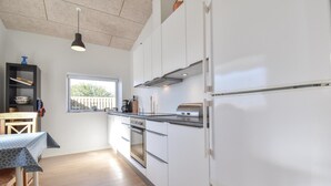 Une cuisine moderne avec des meubles blancs, un réfrigérateur en acier inoxydable et une fenêtre donnant sur une terrasse en bois.