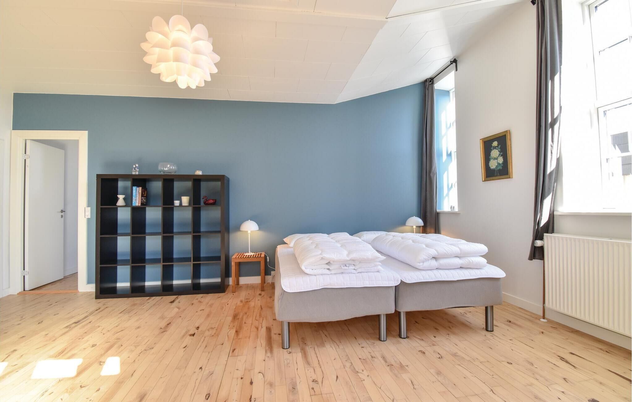 Une chambre à coucher avec un lit double, une petite table de chevet, une lampe sur pied, une bibliothèque et un luminaire au plafond.