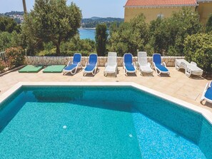 Una piscina con agua azul, rodeada de sillas de descanso y un muro de piedra.