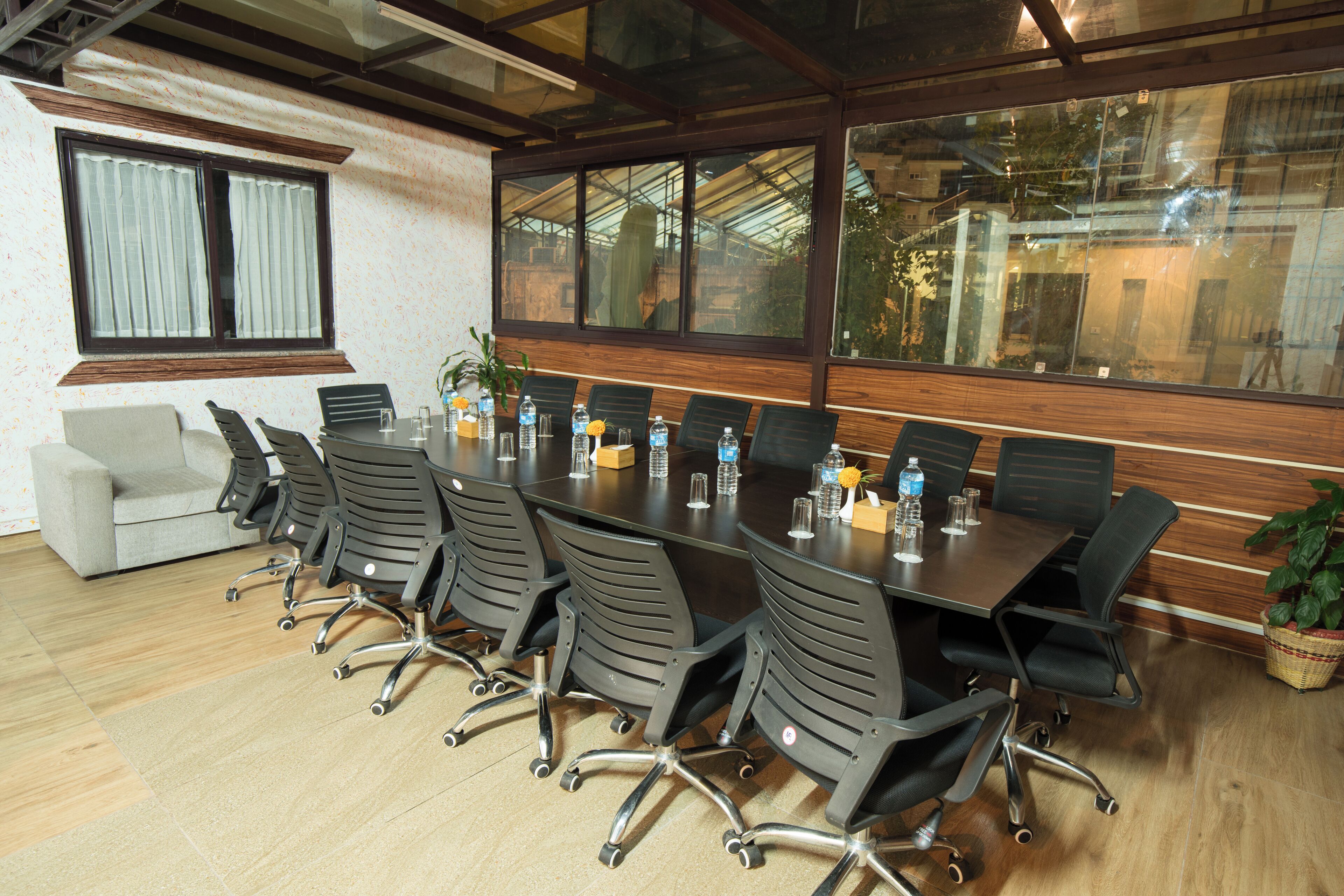Une salle de conférence avec une longue table, de nombreuses chaises, un canapé et une grande fenêtre dont la surface réfléchit la lumière.