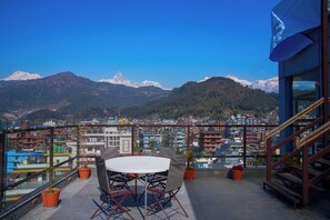 A rooftop terrace with a round table and chairs, potted plants, and a view of a cityscape and mountains. - Hotel Shaara (Pokhara)