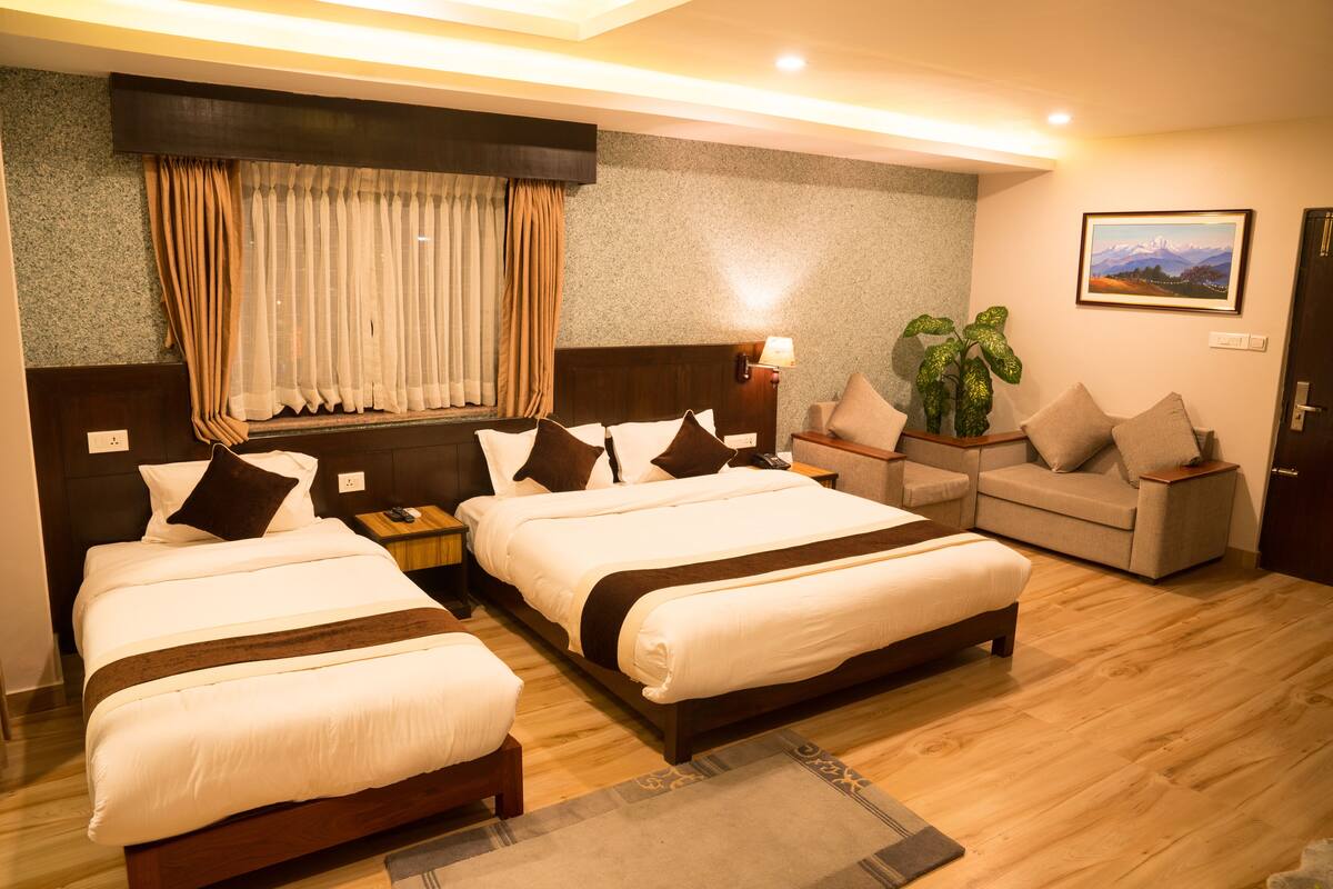 Habitación de hotel con dos camas, un sofá, una mesita de noche con lámpara y una planta en maceta.