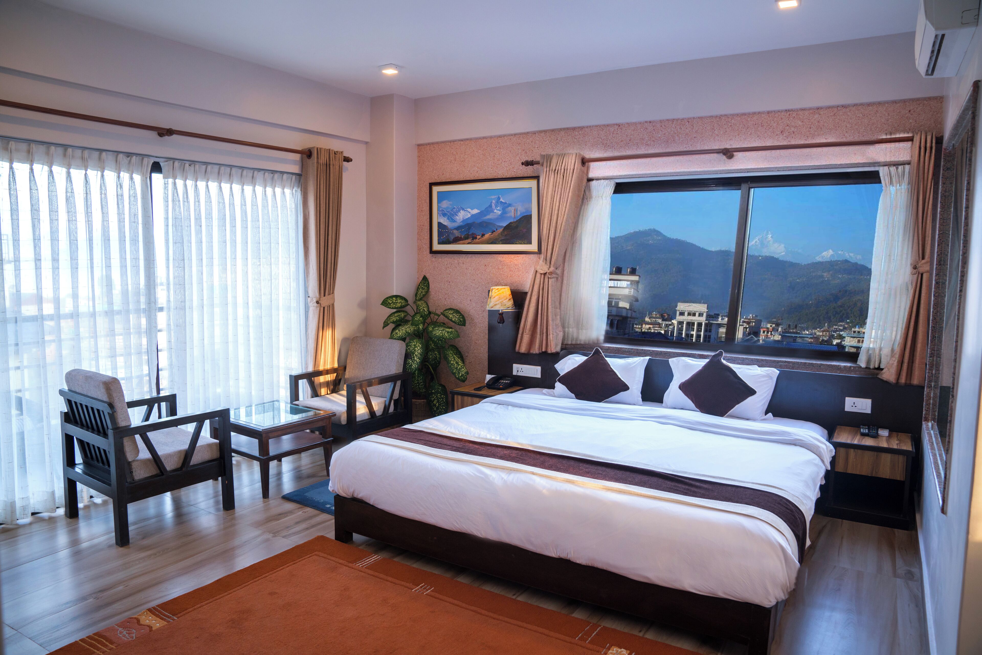 Une chambre d’hôtel avec un grand lit, un bureau avec une chaise, une plante en pot et une fenêtre donnant sur la montagne.