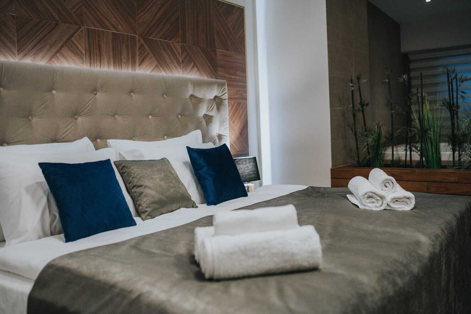 A neatly made bed with a tufted headboard, white and blue pillows, and a folded towel on the bed.