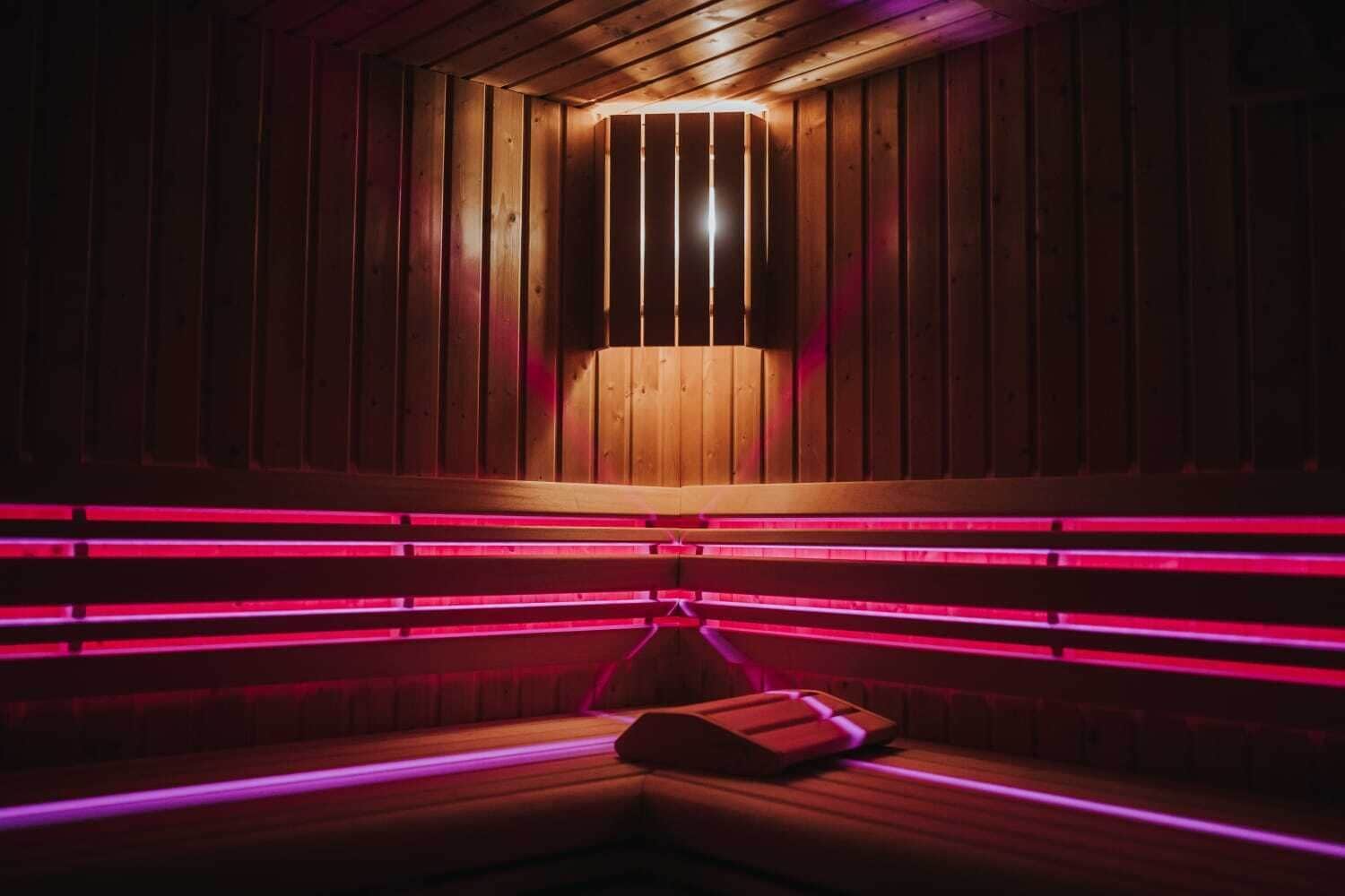 A sauna with wooden walls and benches, illuminated by red lighting.