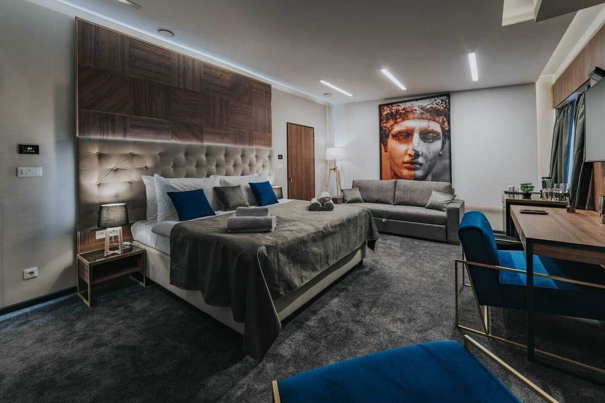A modern bedroom with a large bed, a sofa, a desk, and a large painting on the wall.