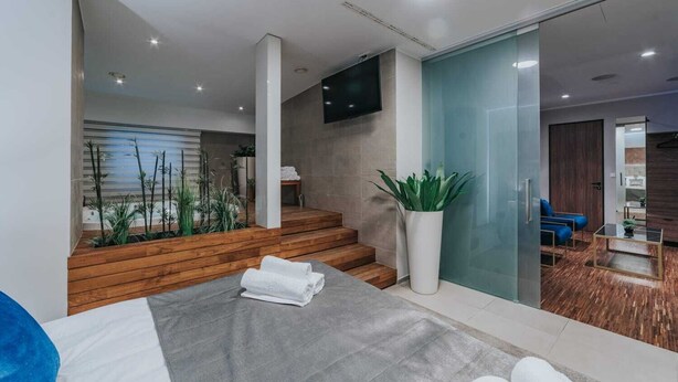 Ein modernes Interieur mit einer Treppe, die zu einem Balkon führt, einer Sitzecke mit Sofa und Couchtisch sowie einer großen Kühlpflanze.