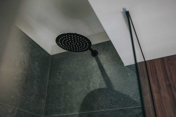 A showerhead in a bathroom with dark tiles and a wooden floor. - Ilica Luxury Center (Zagreb)