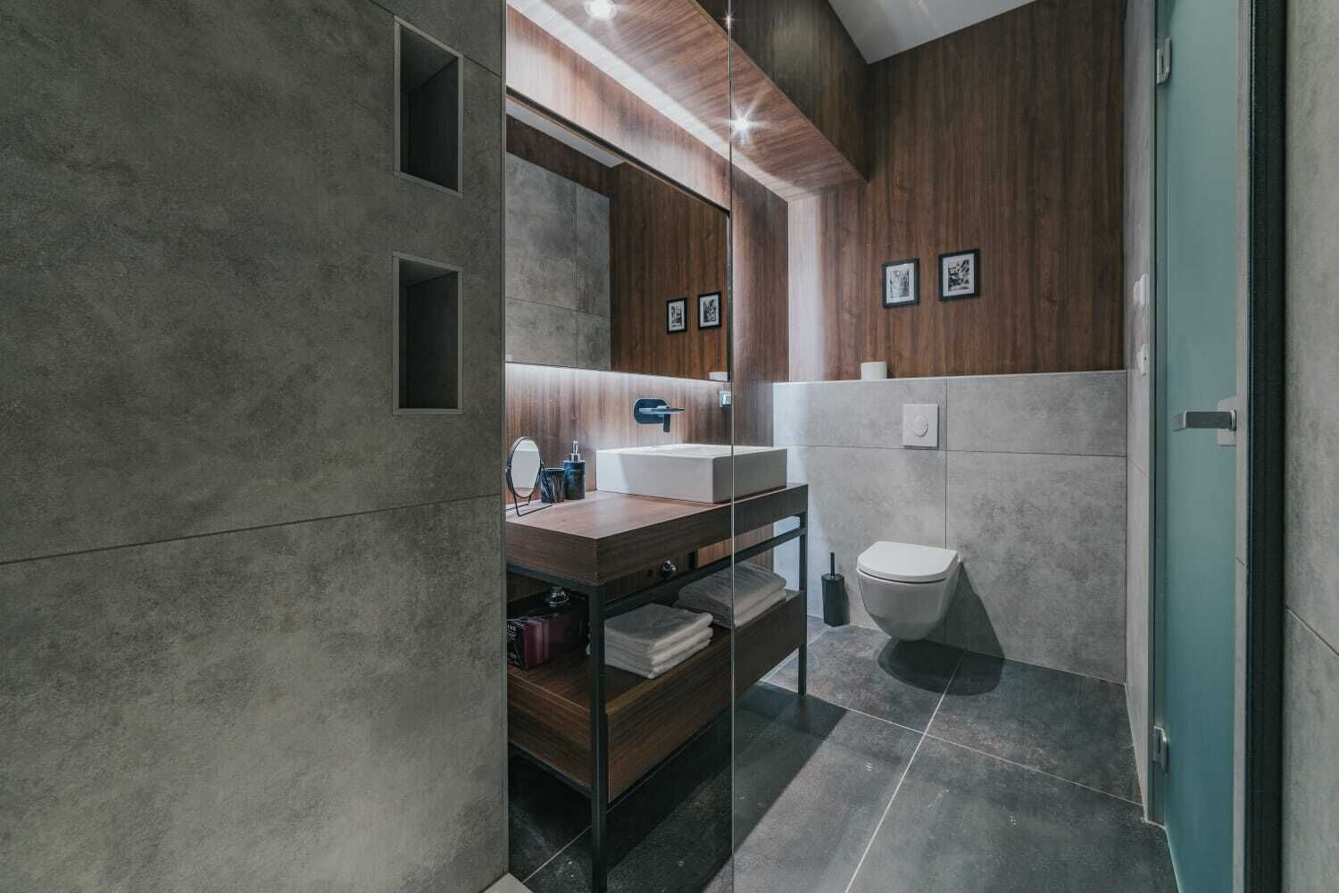 A modern bathroom with a wooden vanity, a mirror, and a toilet.