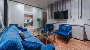 Ein modernes Wohnzimmer mit einer Couch, zwei Sesseln, einem Couchtisch und einem an der Wand montierten Fernseher.