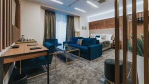 Ein modernes Hotelzimmer mit einem Holztisch, einem blauen Sofa und einem Bett mit einem Holz-Kopfteil.