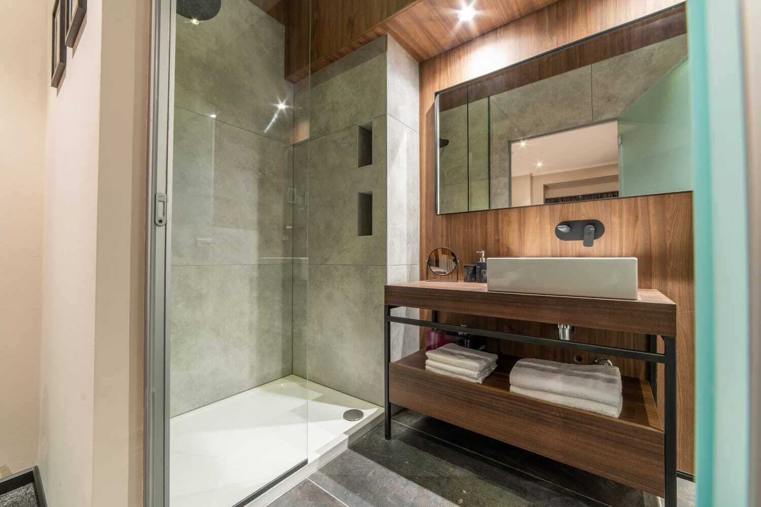 Ein modernes Badezimmer mit Duschkabine aus Glas, einem Holzwaschtisch mit Spiegel und integriertem Waschbecken.