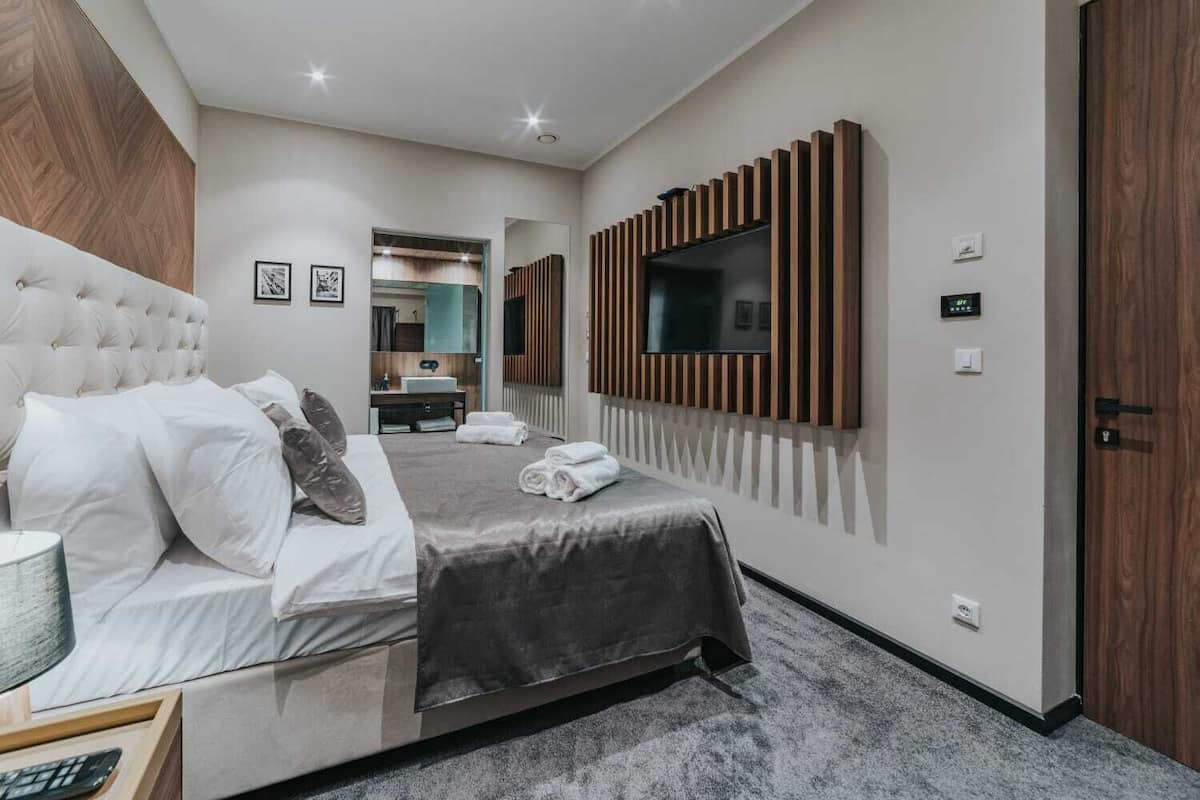 A modern hotel room with a large bed, a TV mounted on the wall, and a wooden door.