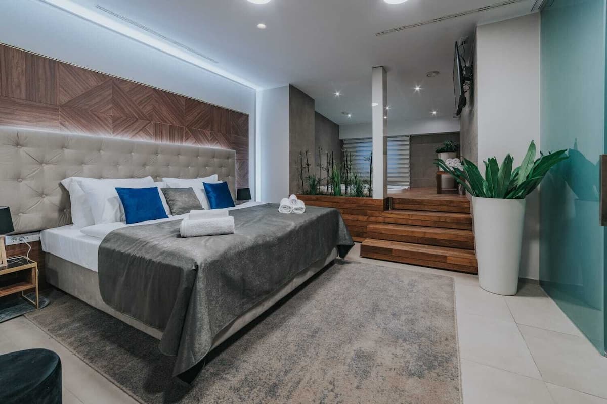 A modern bedroom with a tufted headboard, a large bed with a grey bedspread, and a staircase leading to an upper level.
