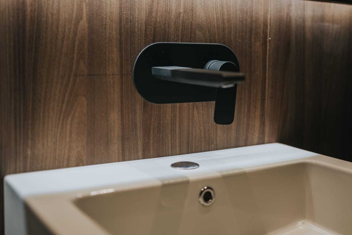 A bathroom sink with a modern faucet and a wooden panel background.