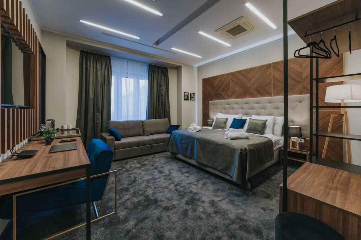 A modern hotel room with a bed, a sofa, a desk, and a chair.