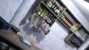 En bar med træbordplade, barstole og en hylde med flasker.