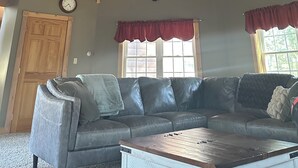 Una habitación con techo de madera, una gran araña con ruedas de madera, un sofá de cuero, una mesa de centro de madera y una ventana con vistas.