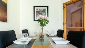 Een eettafel met een bloemenvaas, twee wijnglazen en zwarte stoelen.