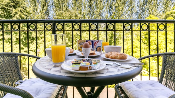 Een balkon met een tafel gedekt voor het ontbijt, inclusief borden met eten, een glas jus d'orange en een beker.