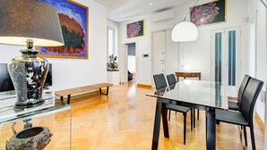 A modern dining area with a glass table, black chairs, a marble vase, and artwork on the walls. - Colosseum Terrace Apartment (Rome)
