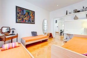 A modern bedroom with two single beds, a wooden dresser, a mirror, a colorful painting, and a shelf with decorative items.