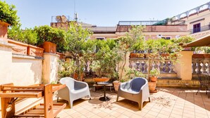 A sunlit patio with two white chairs, a wooden drying rack, and potted plants. - Colosseum Terrace Apartment (Rome)