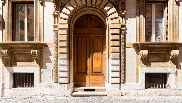 A historic building with a large wooden double door, stone columns, and a cobblestone street. - Colosseum Terrace Apartment (Rome)