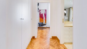 A hallway with a wooden herringbone floor, a black chair, and a door with a colorful abstract painting. - Colosseum Terrace Apartment (Rome)
