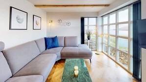 A modern living room with a grey sectional sofa, a green rug, and a large window offering a view of the outdoors. - Gillastova (Frodba)