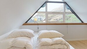 A bedroom with a sloped ceiling and a large triangular window. There are two beds with white bedding and a wooden floor. - Gillastova (Frodba)