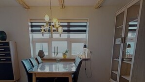 A dining area with a wooden herringbone floor, a glass-top table, and blue chairs. - Gillastova (Frodba)