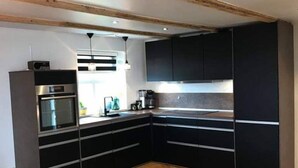 A modern kitchen with dark cabinets, a wooden herringbone floor, and a built-in oven. - Gillastova (Frodba)