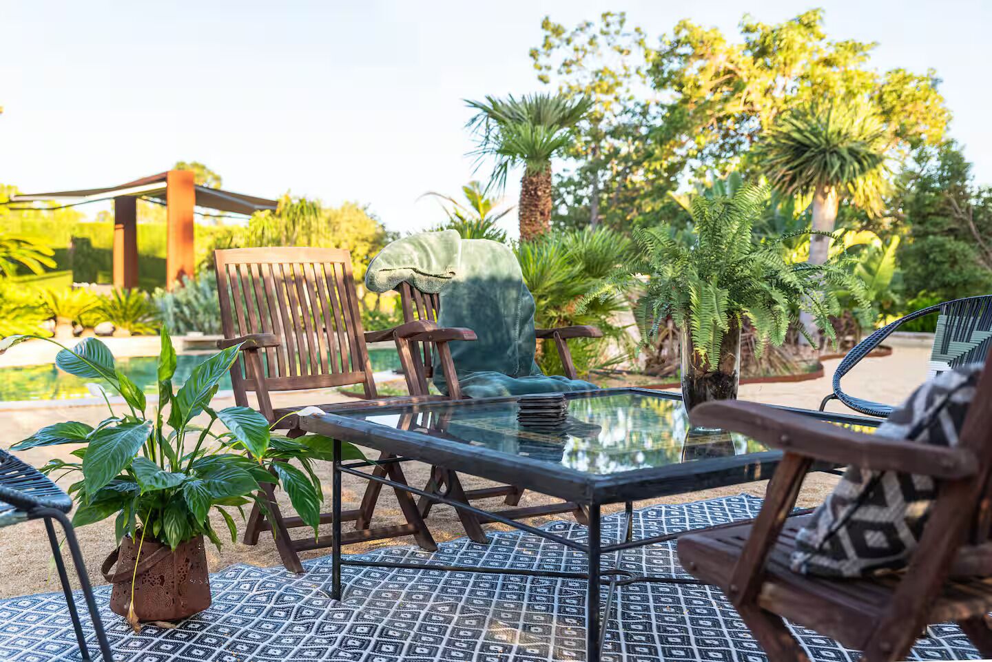 An outdoor seating area with a glass table, wooden chairs, and potted plants.