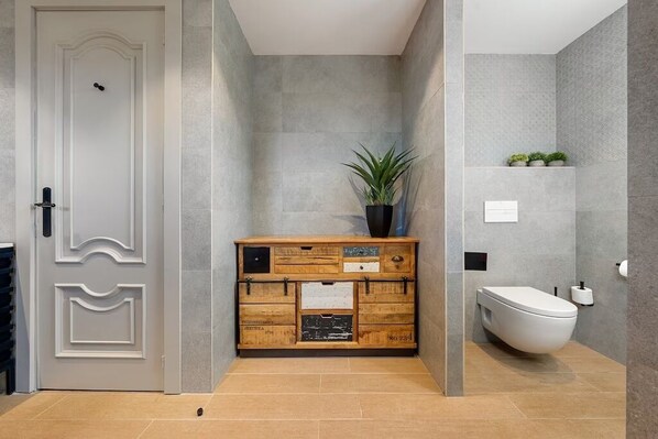 Un baño con un inodoro blanco, un mueble de madera con cajones y una planta en maceta.