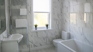 Un bagno con un lavandino bianco, un water, una vasca e una finestra con due piante in vaso.