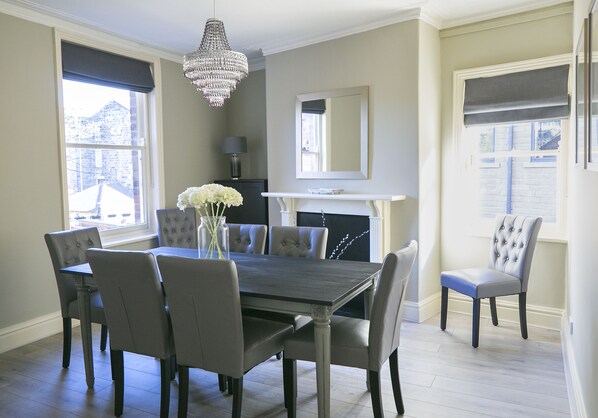 A dining room with a rectangular table, six chairs, a chandelier, and a fireplace.