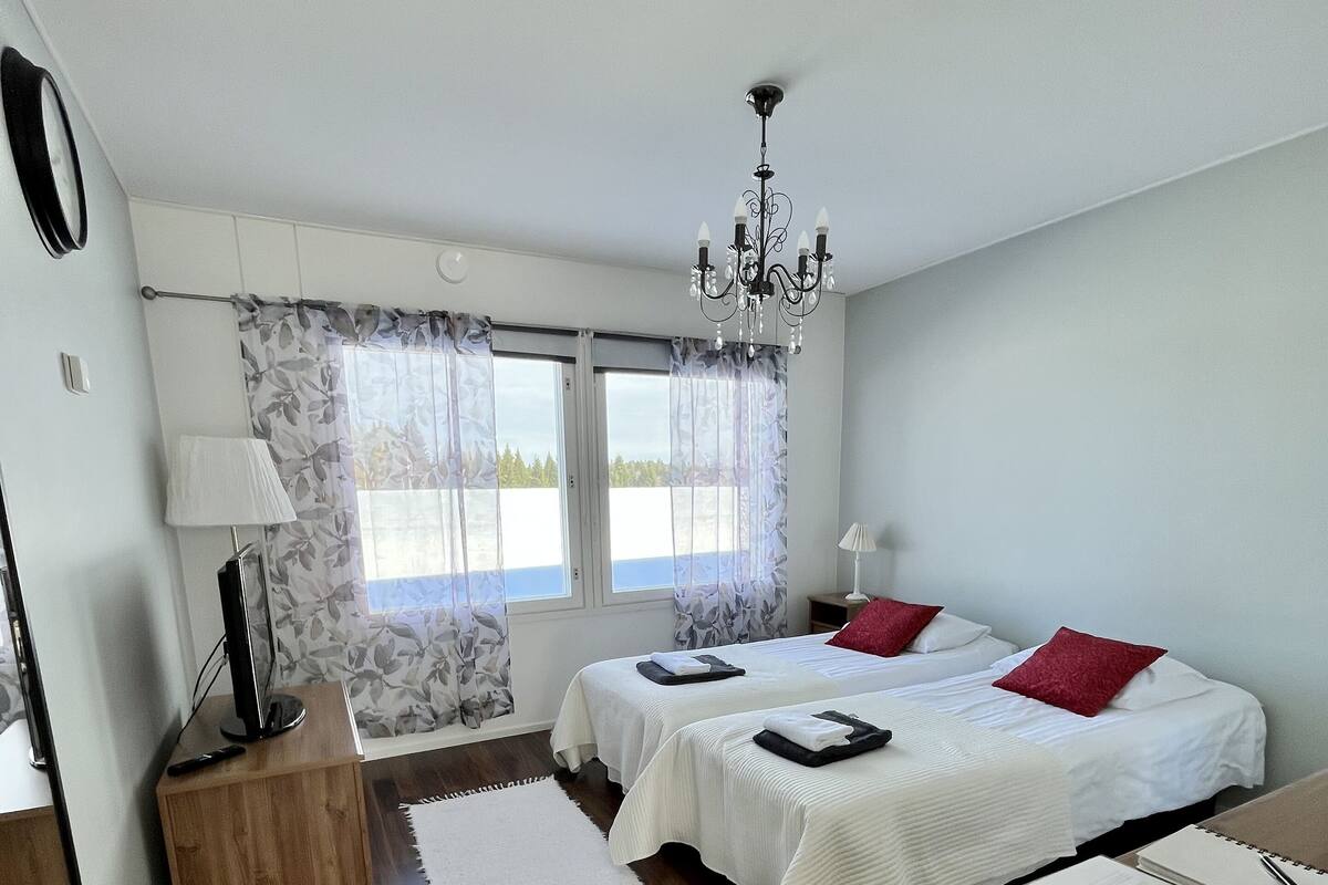 A bedroom with two beds, a chandelier, a desk, and a view of the outdoors.