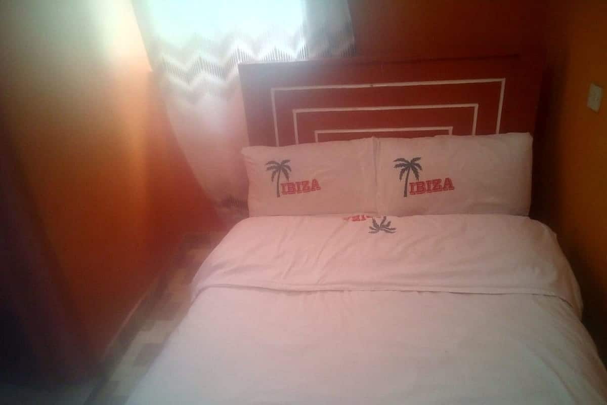 Ein Bett mit weißer Bettwäsche und Kissen mit Palmenmotiven und dem Schriftzug 'IBIZA'.