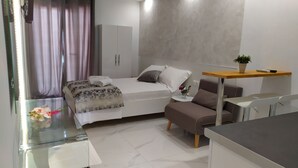 Un dormitorio moderno con una cama, un pequeño sofá, una mesita de noche con una planta y un separador de vidrio.