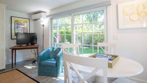 A living room with a television, a blue chair, a white table, and a large window with a view of greenery. - East End Condo w/ Beach Access! (Provincetown)