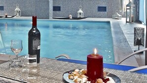 Zona de piscina con mesa lista para comer, una botella de vino y velas.