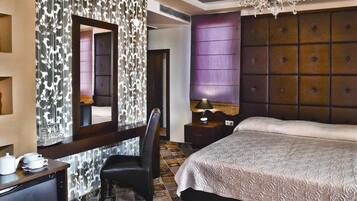 A hotel room with a large bed, a chair, a desk with a lamp, and a mirror.