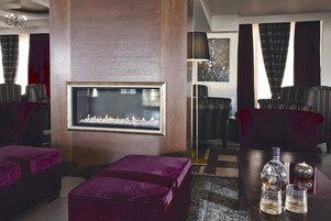 Una sala de estar moderna con chimenea, asientos cómodos y una zona de bar con vasos y botellas.